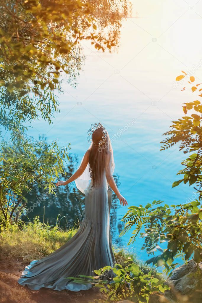 artwork woman queen stands onshore lake. summer sunset sun light. fashion model in gray vintage long dress silhouette mermaid. silver crown. fantasy photography concept divine freedom. Back rear view