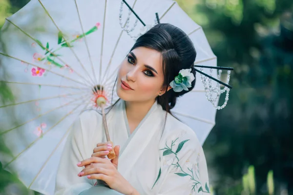 Portré fiatal kelet-ázsiai nő. Gésa lány kezében fehér japán esernyő. Keleti vörös smink szem frizura fekete haj díszített virág matsuba, kanzashi. Kínai nemzeti jelmez kimonó — Stock Fotó