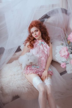 Sanat fotoğraflı kızıl saçlı kadın Barok tarzı fırfırlı iç çamaşırı. Rococo hacimli saç stili. Kanepede beyaz tavşan pozu veren bir kadın var. Seksi yüz pembe karnaval makyajı. Klasik kraliyet odası.