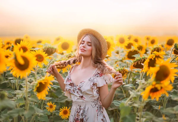 Konstfoto. ung kvinna mode modell njuta av sommar natur solnedgång, står i blommande fält. byn Gula orange blommor solros. Blond flicka som håller två flätor i händerna. Landsbygdsbåt halmhatt — Stockfoto