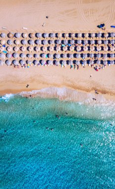 Renkli şemsiyeli kumlu sahil manzarası yazın günbatımında şeffaf mavi suyla deniz koyunda yüzen insanlar. Sahildeki hava manzarası, şemsiyeler, kum ve deniz dalgaları..