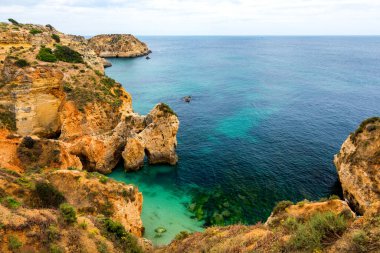 Alvor kasabası, Algarve, Portekiz 'de altın renkli taşlı çarpıcı sahil manzarası. Alvor sahilindeki kayalıkların manzarası, Algarve bölgesi, Portekiz.