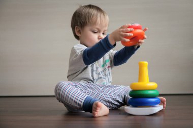 Katta oturan bir çocuk bir çocuk piramit toplar. 
