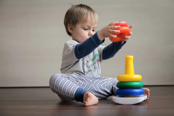 Katta oturan bir çocuk bir çocuk piramit toplar. 