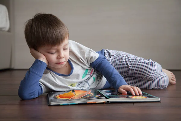 A child lying on the floor looks and reads a book about the cosmos.