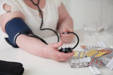 Yaşlı bir kadın masada oturur ve kan basıncını ölçer.