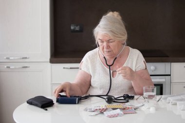 Büyükanne ve tonometer. Emekli masada oturuyor.