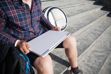 Adam merdivende oturuyordu. Onun yanında onun mono tekerlek var. Elinde bir laptop tutar.