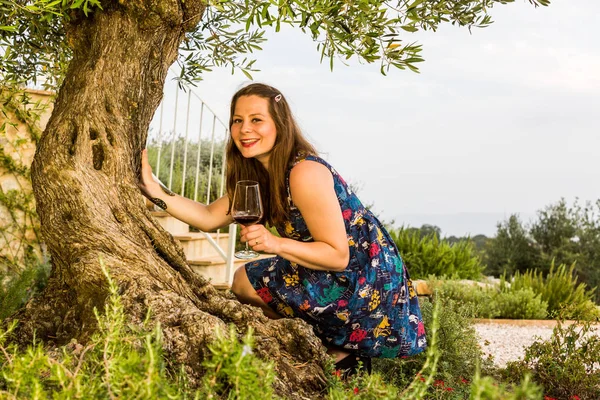 Veduta di una ragazza con un bicchiere di vino in piedi sotto il vecchio ulivo — Foto Stock