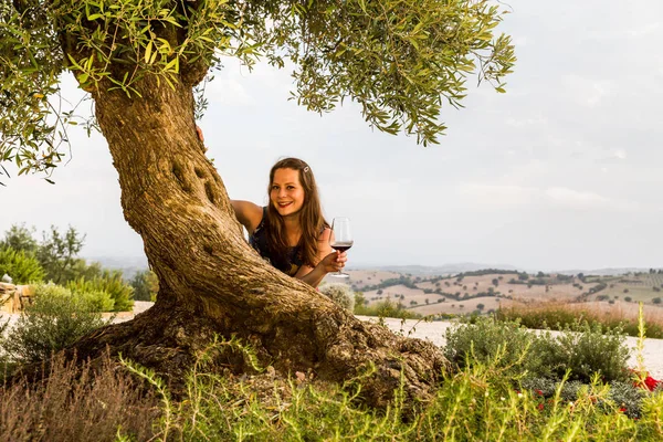 Veduta di una ragazza con un bicchiere di vino in piedi sotto il vecchio ulivo — Foto Stock