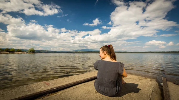 Menina sentada perto da água no lago barreira Oravska Priehrada no norte da Eslováquia — Fotografia de Stock