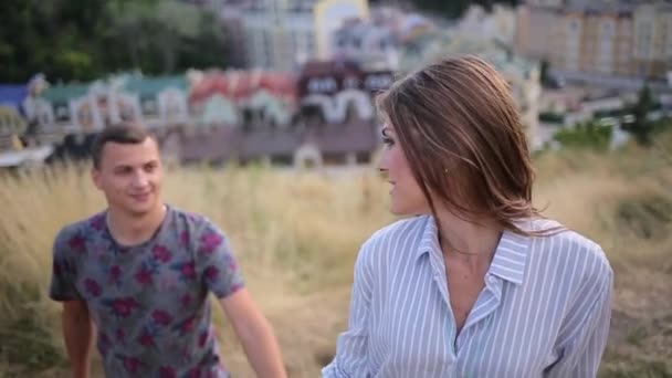 Пара поднимается на холм на фоне города — стоковое видео