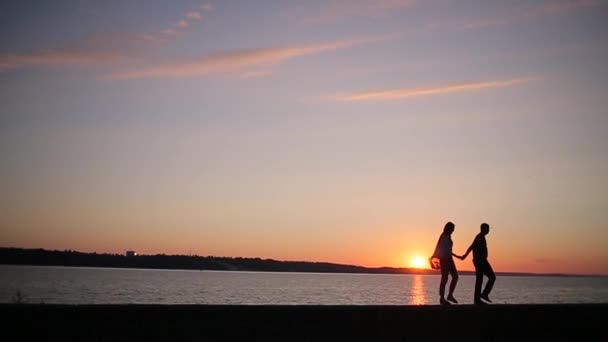 Pareja está caminando en la orilla del río al atardecer — Vídeos de Stock