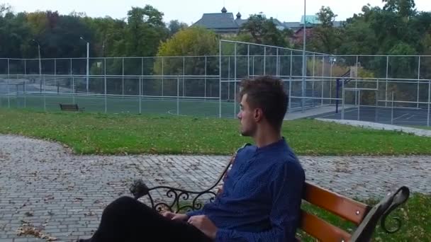 Homem sentado em um banco perto do parque infantil — Vídeo de Stock