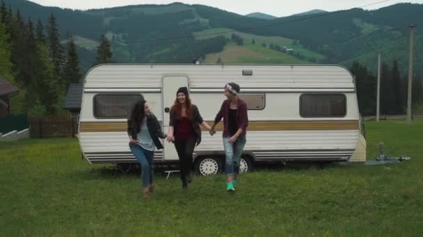 Девушки идут, держась за руки возле трейлера в горах — стоковое видео