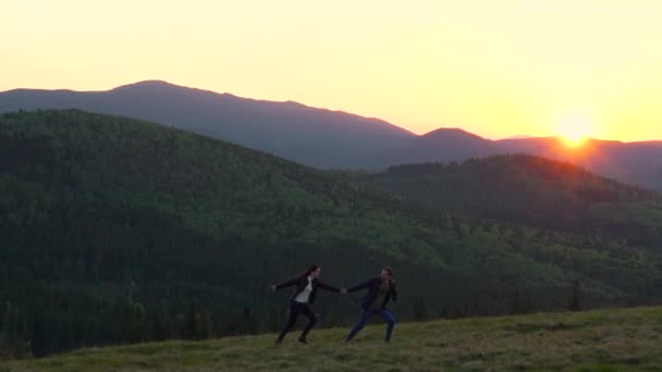Dağlarda günbatımı karşı çalışan çift — Stok video