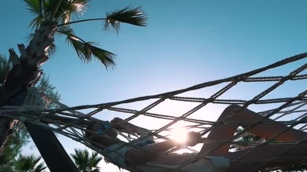 Het meisje ontspant in een hangmat in de buurt van de palmen — Stockvideo
