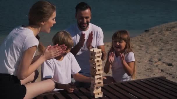 Familia feliz juega jenga juego cerca del lago — Vídeo de stock