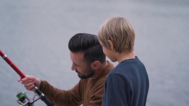 爸爸教他的儿子如何处理鱼竿 — 图库视频影像