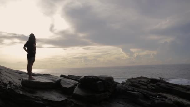 Дівчина стоїть на скелях біля океану — стокове відео