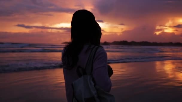 Το κορίτσι με το σακίδιο στο ηλιοβασίλεμα κοντά στον ωκεανό — Αρχείο Βίντεο