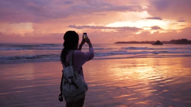 Menina tira uma foto do belo pôr do sol pelo oceano — Vídeo de Stock