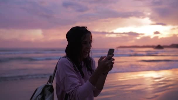 Dívka bere selfie v blízkosti oceánu při západu slunce — Stock video