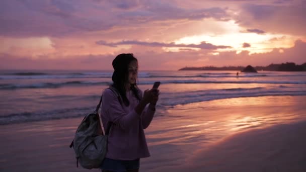 Girl types a message near ocean at sunset — Stock Video