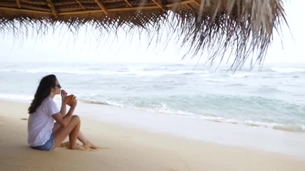 La fille boit un cocktail et regarde les vagues — Video