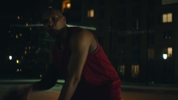 Mężczyzna gra w koszykówkę uliczną z nocnymi światłami — Wideo stockowe