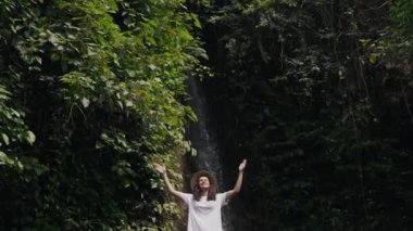 Kız ellerini şelalenin arka planında kaldırır.