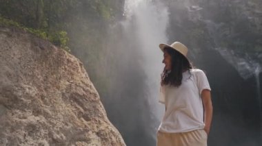 Şelalenin arka planında gülümseyen turist kız.