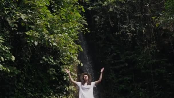 Menina levanta as mãos no fundo de uma cachoeira — Vídeo de Stock
