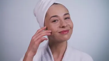 Bornozlu kız yüzüne yakından dokunuyor.