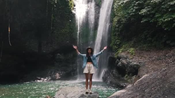 Fille lève les mains au-dessus d'elle-même sur le fond d'une cascade — Video