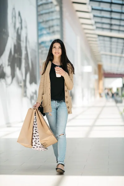 Alışveriş torbaları ve onun elinde sıcak içecek ile çekici sevimli kız — Stok fotoğraf
