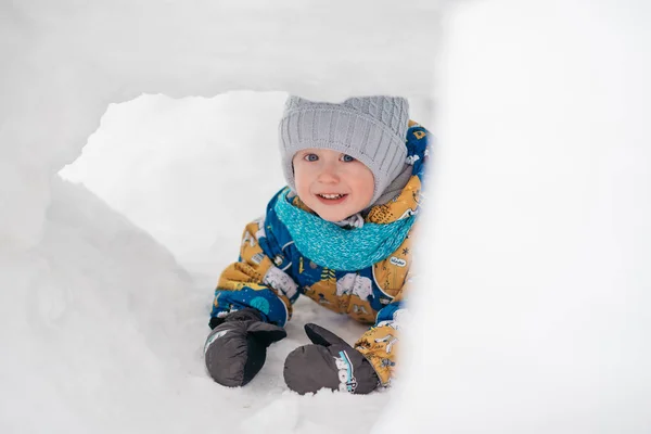 Lindo niño está jugando al aire libre en iglú túnel fuerte cavó en la pila de nieve en el día de invierno . Imágenes de stock libres de derechos
