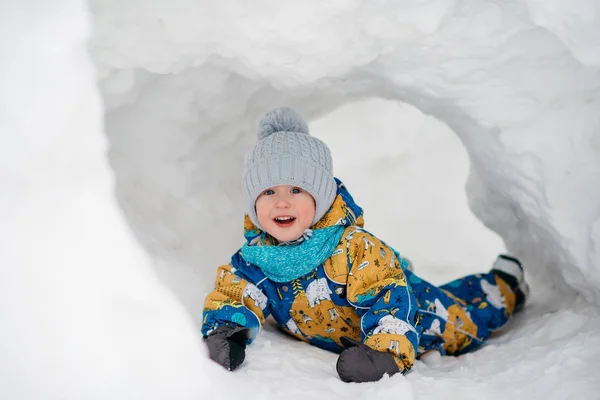 Lindo niño está jugando al aire libre en iglú túnel fuerte cavó en la pila de nieve en el día de invierno . Fotos de stock