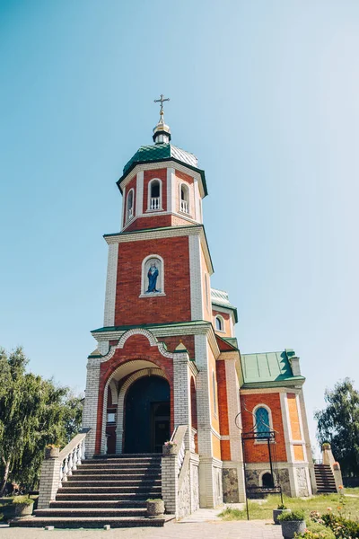 Küçük bir tuğla kilise, yeşil kubbesi ve altın haçı olan bir tapınak.