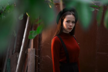 Koyu kırmızı zemin üzerine poz adı ne? Model giyen şık şapka çapında ekledi. Kız kameraya benziyor. Kadın moda. Tonda