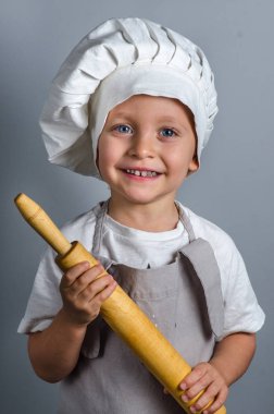 Smiling little cook with rolling pin, isolated on gray background
