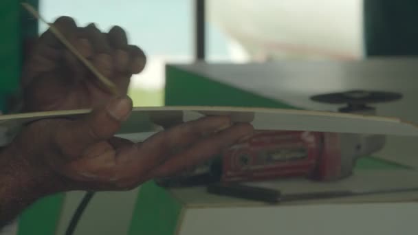 Крупним планом рука молодої людини малює дерев'яну частину човна в гавані . — стокове відео