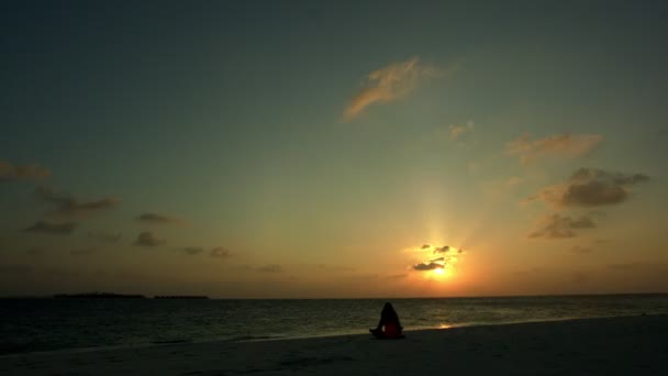 Time lapse de fille de yoga assis sur le fond de ciel orangé violet foncé coloré coucher de soleil sur l'océan aux Maldives. — Video