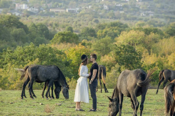 Hermosa pareja joven que se queda y se besa cerca de caballos . —  Fotos de Stock