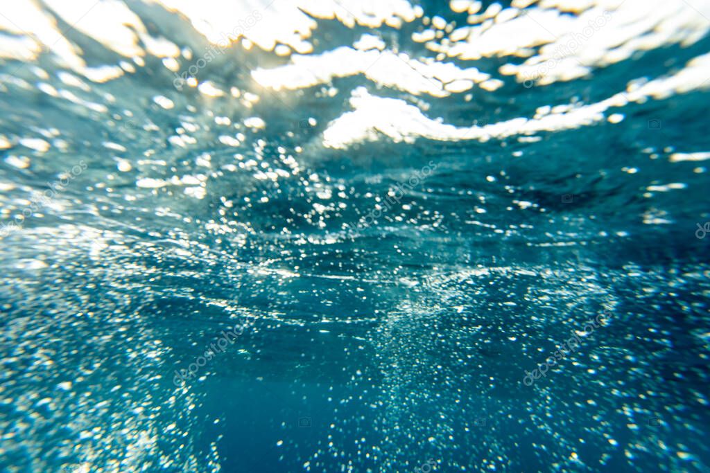Underwater background of deep turquoise and blue ocean water with beams of sunlight refracting through the surface.