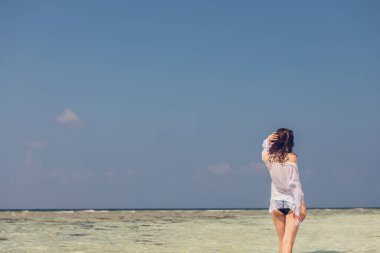 Beyaz elbiseli, kumsalda kollarını kaldırıp okyanusun tadını çıkaran, yaz esintisi ve tatilde dalgaların sesini dinleyen neşeli ve çekici genç bir kadın. İyi tatiller..