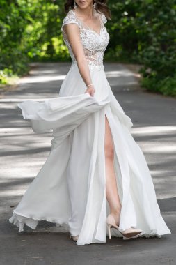 wedding dress with a long slit for legs and lace top. The bride walks in the park in a beautiful white dress. The wedding dress flutters in the wind while walking through the park.