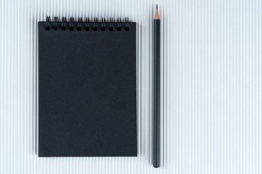 Siyah defter ve siyah kalem, beyaz karton kaplama arka planda. Siyah kâğıt ve beyaz kalemin kıvrımlı karton zemin üzerinde yattığı notları düzenle. Boşluğu kopyala.