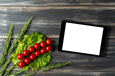 Çeri domatesleri, marul, biberiye ve tablet bilgisayar. Siyah ahşap masaya. Salata tarifi, vejetaryen menüsü