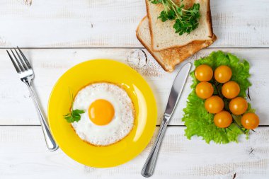 Sarı tabakta kızarmış yumurta, kiraz domatesli marul ve tost. Hafif kahvaltı..